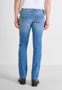 Jeans in denim blu con un taglio dritto, caratterizzati da un lavaggio sbiadito, tasche posteriori e una leggera elasticità. I dettagli includono cuciture visibili e passanti per cintura.