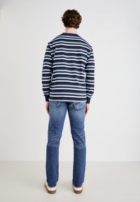 Camisa de manga larga a rayas en azul marino y azul claro, de material de algodón, con cuello redondo, combinada con vaqueros rectos desgastados en azul y zapatillas ligeras.