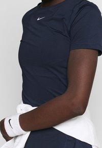 Mörkblå sporttröja med korta ärmar och rund halsringning, med en liten vit Nike-logotyp på bröstet, kombinerad med ett vitt midjeband.