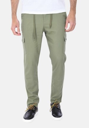 Uomo che indossa pantaloni cargo verde oliva con tasche laterali e vita con coulisse, abbinati a scarpe nere con suola bianca.