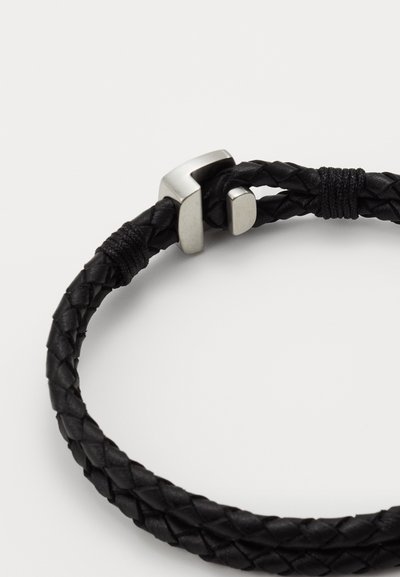Bracelet en cuir tressé noir avec un fermoir métallique en argent élégant. Présente une finition texturée et un design simple et sans embellissement.