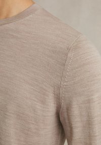 Lichtbruine langemouwen shirt met een ribbelrand bij de hals, zachte textuur en zichtbare stikseldetails op de schouders en zijnaad.