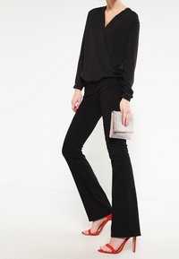 Svart blus med V-ringning, parat med svarta utsvängda byxor. Accessoarer inkluderar en clutch med silverpärlor och röda högklackade sandaler.