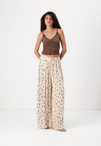 Haut court marron smocké avec des bretelles fines, associé à un pantalon large beige à motif noir et taille à cordon. Texture de tissu lisse.