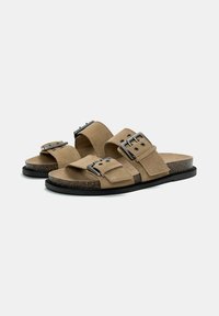 Braune Wildledersandalen mit zwei breiten Riemen, ausgestattet mit metallischen Schnallen, Korkfußbett und schwarzer Gummisohle. Einfaches, flaches Design.