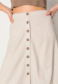 Saia beige clara feita de um tecido suave e texturizado, apresentando um fecho frontal com sete botões de madeira para um detalhe adicional.