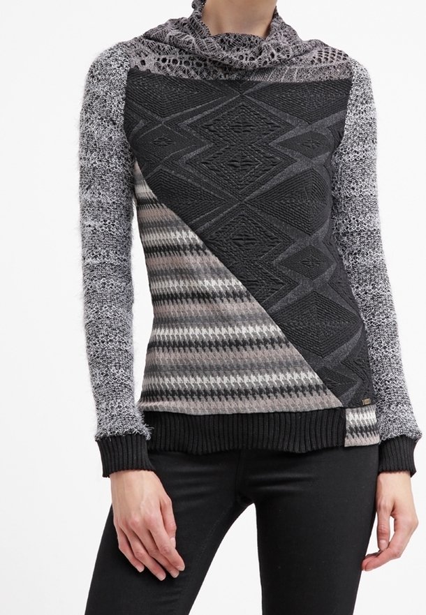 Pull en tricot avec un design mixte comportant des motifs géométriques en noir, gris et blanc. Col montant, manches longues et poignets côtelés.