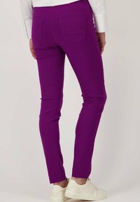 Vibrante paarse strakke broek met een gladde textuur, voorzien van twee achterzakken en subtiele logo-details. Gepaard met witte schoenen.