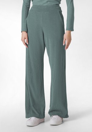 Helle grüne weit geschnittene Hose aus strukturiertem Stoff, mit hoher Taille und seitlichen Taschen, kombiniert mit weißen Sneakers.