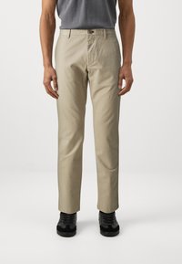 Beige chinos with a straight-leg design, featuring a button closure, side pockets, and worn with black sneakers. Smooth, durable fabric.