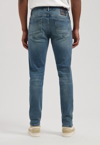 Jeans din denim cu croi slim, cu talie medie, de culoare albastru deschis, cu zone estompate. Au două buzunare pe spate și un mic eticheta de marcă pe talie.
