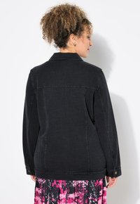 Svart denimjacka med krage och detaljer med knäppning på ärmarna, med en texturerad yta och en figursydd passform, bärs över en mönstrad kjol.