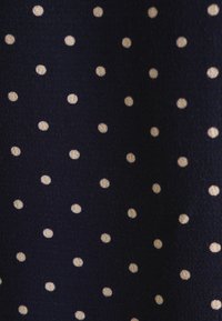 Tessuto blu navy con pois beige piccoli e uniformemente distribuiti. La texture appare liscia con una leggera lucentezza.