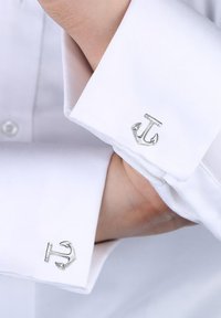 Silver ankarlänkar på en vit skjorta. Länkarna har en polerad metallfinish med en detaljerad ankardesign.