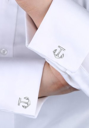 Sølv anker manchetknapper på en hvid skjorte. Manchetknapperne har en poleret metallisk finish med et detaljeret ankerdesign.