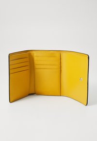 L'intérieur du portefeuille en cuir jaune présente plusieurs emplacements pour cartes et une fermeture à pression, avec une texture lisse et des bords noirs contrastants.