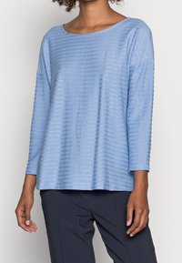 Jasnoniebieska bluzka z długim rękawem o luźnym kroju, z poziomymi paskami i okrągłym dekoltem. Miękki materiał o subtelnej teksturze.