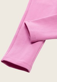 Figurbetonte rosa Baumwollleggings mit glatter Textur und verstärktem Saum, die aus einer Nahaufnahme einen Teil des Beins und des Ärmels zeigen.