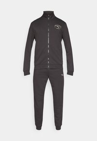 Γκρι αθλητική φόρμα, που περιλαμβάνει ζακέτα με φερμουάρ και ψηλό γιακά με ριμπ μανσέτες, καθώς και αντίστοιχο στενό παντελόνι με εφαρμοστά μπατζάκια.