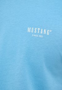 Light blue cotton T-shirt featuring the text "MUSTANG" and "SINCE 1932" in white. Simple, smooth texture with a classic crew neck design.