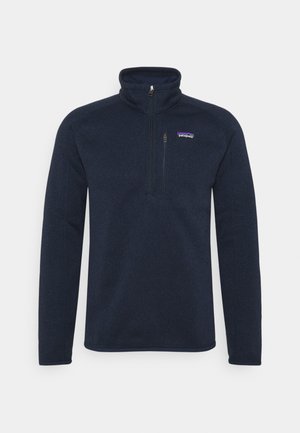 Sudadera de forro polar de un azul marino oscuro con un alto cuello, cierre de media cremallera y un pequeño logo en el lado izquierdo del pecho. Textura suave, mangas ajustadas.