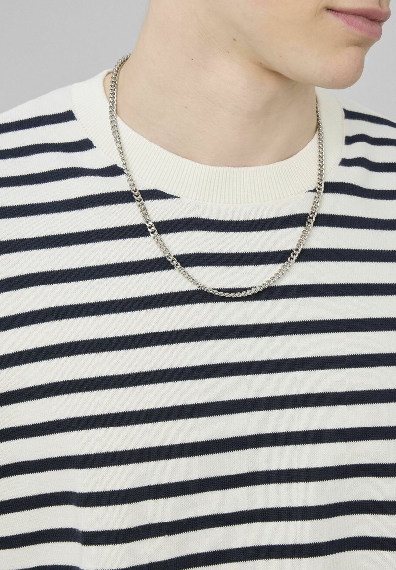 Homme portant une chaîne en argent sur un t-shirt à rayures horizontales blanches et noires avec un col rond.