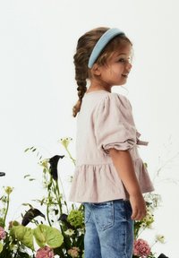 Světle růžový, strukturovaný peplum top s balónovými rukávy, ve spojení s modrými džínami. Dítě s pleteným účesem a modrým čelenkou.