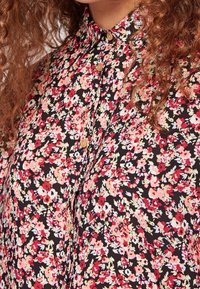 Camicia a maniche corte con bottoni, a sfondo nero, decorata con fiori rossi, rosa e bianchi, e colletto classico. Tessuto morbido e testurizzato.