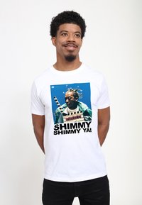 Hvid bomulds t-shirt med et grafisk print af en person med fletninger, iført en grøn jakke og en filmklapper. Teksten siger "SHIMMY SHIMMY YA!"