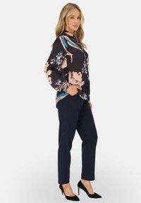 Granatowa bluzka w kwiaty z różowymi i niebieskimi wzorami, z kołnierzykiem, długie rękawy. Zestawiona z dopasowanymi granatowymi spodniami i czarnymi szpilkami.