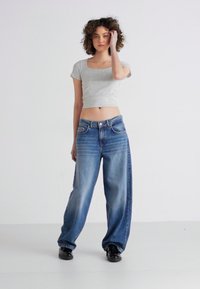 Grå, kort t-skjorte paret med lyseblå, løse jeans. Jeansene har falming og en rett ben-design med lommer.