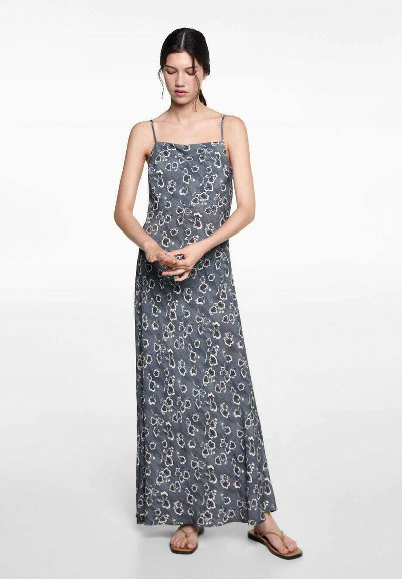 Maxiklänning i grått med blommönster, spagettistlutsar och en svängig design. Tyget verkar lätt och mjukt, i kombination med platta sandaler.