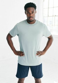 Helles graues, kurzärmliges Sportshirt mit strukturiertem Finish, kombiniert mit dunkelblauen Shorts. Die Passform ist entspannt, mit einem Rundhalsausschnitt.