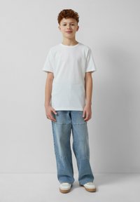 Witte t-shirt met korte mouwen, gecombineerd met lichtblauwe wijde jeans met zichtbare stiksels, en witte sneakers met beige zolen.