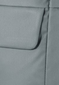 Gros plan sur une poche en tissu gris clair avec rabat, montrant la texture détaillée et les coutures sur un matériau doux.