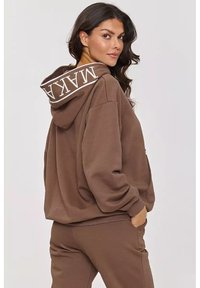 Brązowy hoodie z podwójnym kapturem, w oversize'owym kroju i z logo na kapturem. Posiada ściągacze przy mankietach oraz przednią kieszeń.