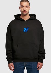 Schwarzer Hoodie mit einer Fronttasche, ausgestattet mit einer blauen Schmetterlingsstickerei auf der Brust. Der Stoff wirkt weich und strukturiert, lässige Passform.