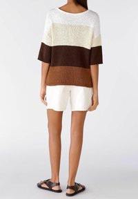 Suéter de punto con un escote amplio, que presenta rayas horizontales en crema, beige, marrón y marrón oscuro. Combinado con pantalones cortos blancos y sandalias negras.
