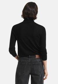Zwarte coltrui met lange mouwen, zachte textuur, aansluitend ontwerp. Gecombineerd met hoogdrachtige donkergrijze jeans met achterzakken.