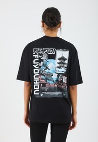 Juoda marškinėliai su dideliu grafinio vaizdo atspaudą ant nugaros, kuriame pavaizduota tradicinė japonų architektūra, Fujis kalnas ir stilizuotas tekstas.