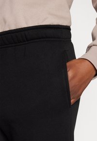 Svarta joggingsbyxor med resårmidja och sidofickor, med en slät yta; kombinerat med en ljusfärgad långärmad topp.