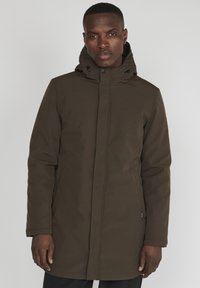 Jachetă parka maro cu glugă, din material impermeabil, croială dreaptă, cu buzunare laterale și o glugă reglabilă cu detalii de strângere.