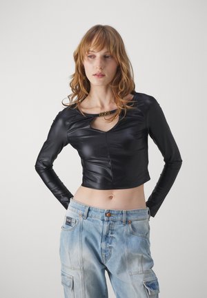 Top nero cropped a maniche lunghe realizzato in pelle liscia, con scollatura ampia e un piccolo taglio, abbinato a jeans cargo blu sbiaditi.