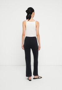 Calças pretas de sino com uma textura suave, emparelhadas com uma t-shirt justa branca de alças finas. Design simples e minimalista.