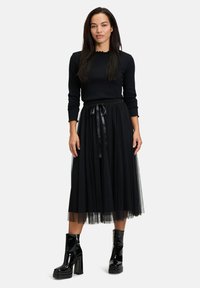 Gonna in tulle nera con cintura elastica e fiocco in satin, abbinata a un top nero a maniche lunghe. Stivali neri con plateau lucidi completano l'outfit.