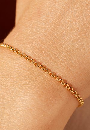 Gouden kettingarmband, met ronde schakels, een gladde textuur en een delicate uitstraling, die op een huidkleurige pols ligt.