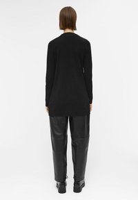 Pull noir à manches longues avec un design droit, porté avec un pantalon en cuir noir taille haute et des chaussures noires épaisses. Aucun motif visible.