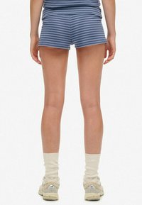 Shorts blu a righe realizzati in tessuto morbido, con un design aderente. Indossati con calzini color crema e sneakers chiare.