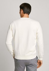 Sudadera color crema con mangas largas y cuello redondo, que presenta una textura suave y puños y dobladillo acanalados.