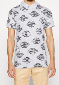 Piké skjorta i lätt tyg med vit bakgrund och upprepande svart glob- och varumärkeslogomönster. Kortsleeves, klassisk krage.